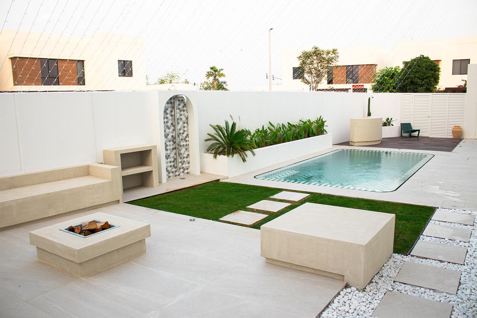 Villa courtyard with built-in seating, decorative wall screens and a fire table beside the pool, built by Eagle in Abu Dhabi