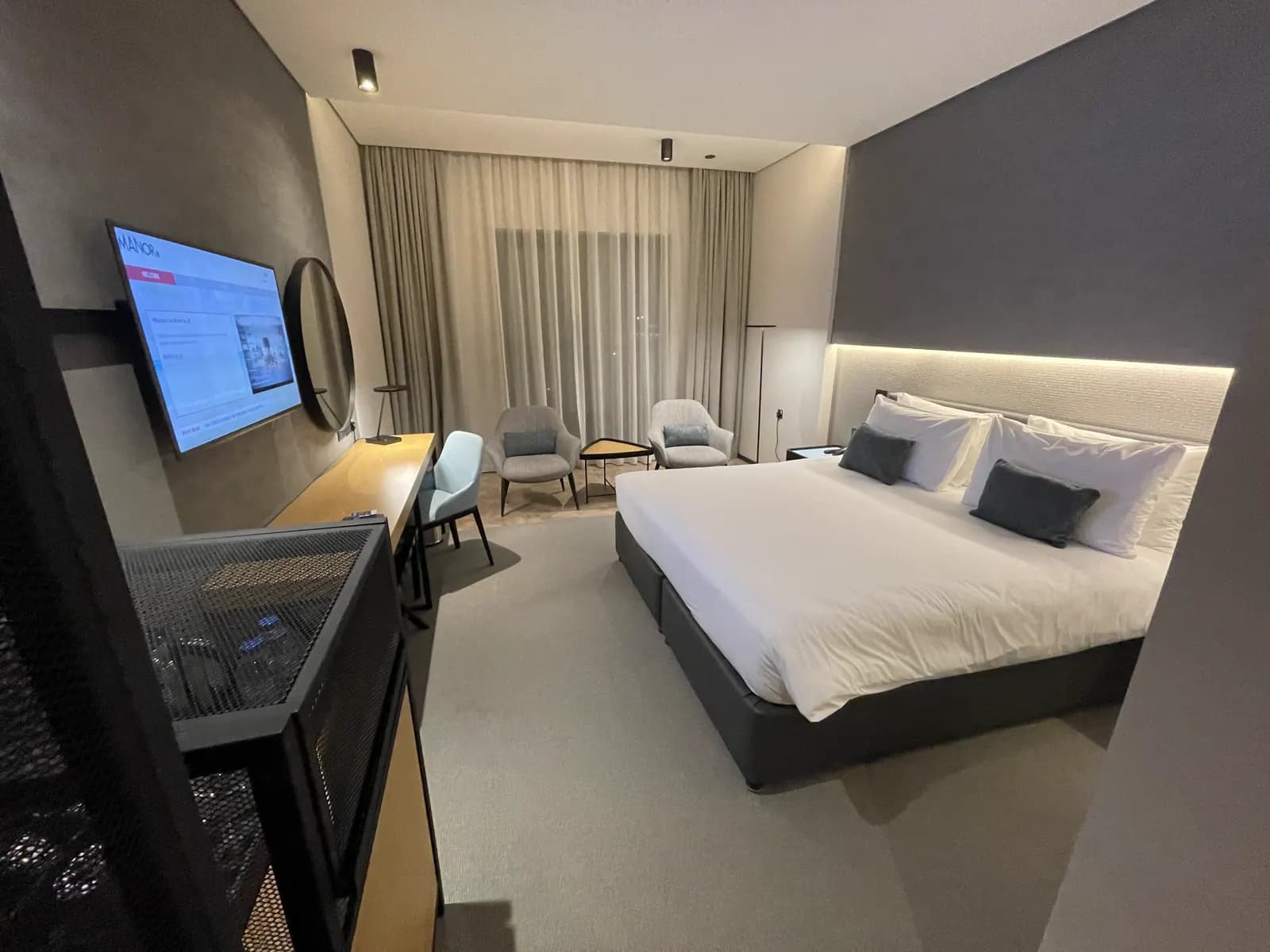 Hotel bedroom with upholstered headboard, wall-mounted display and sheer curtains