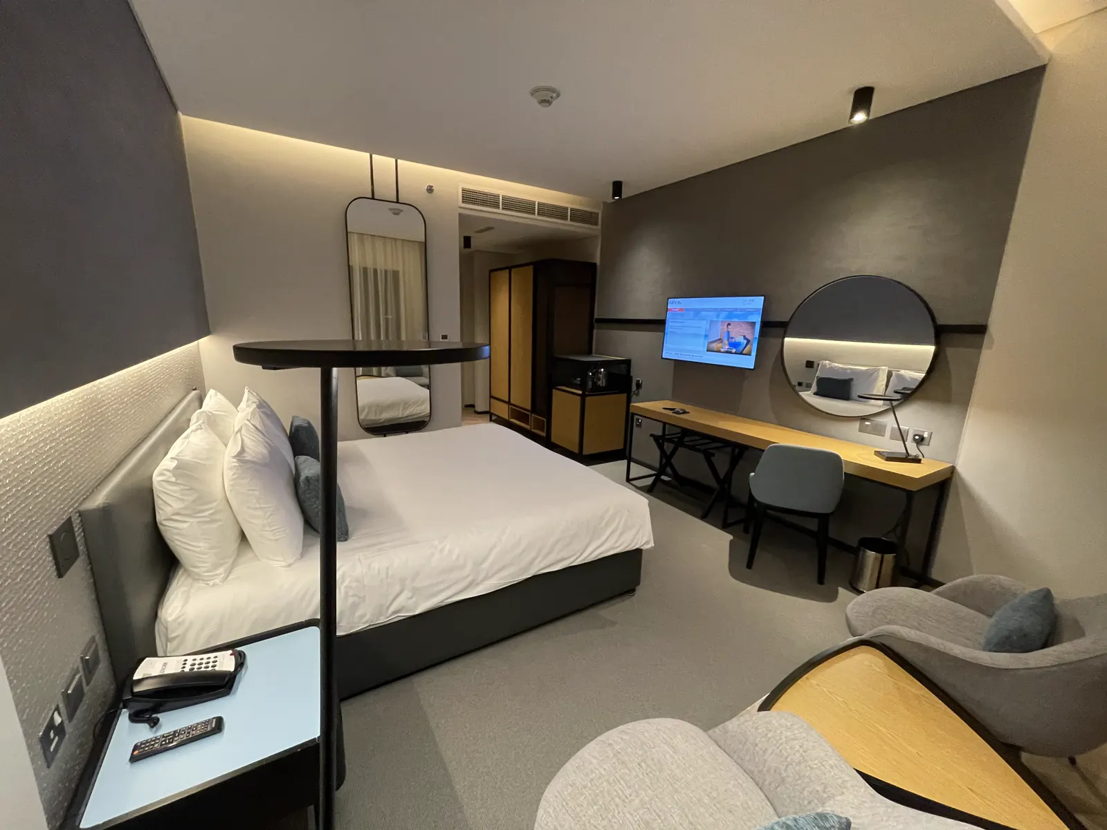 Hotel room with work desk, round mirror and integrated bedside joinery