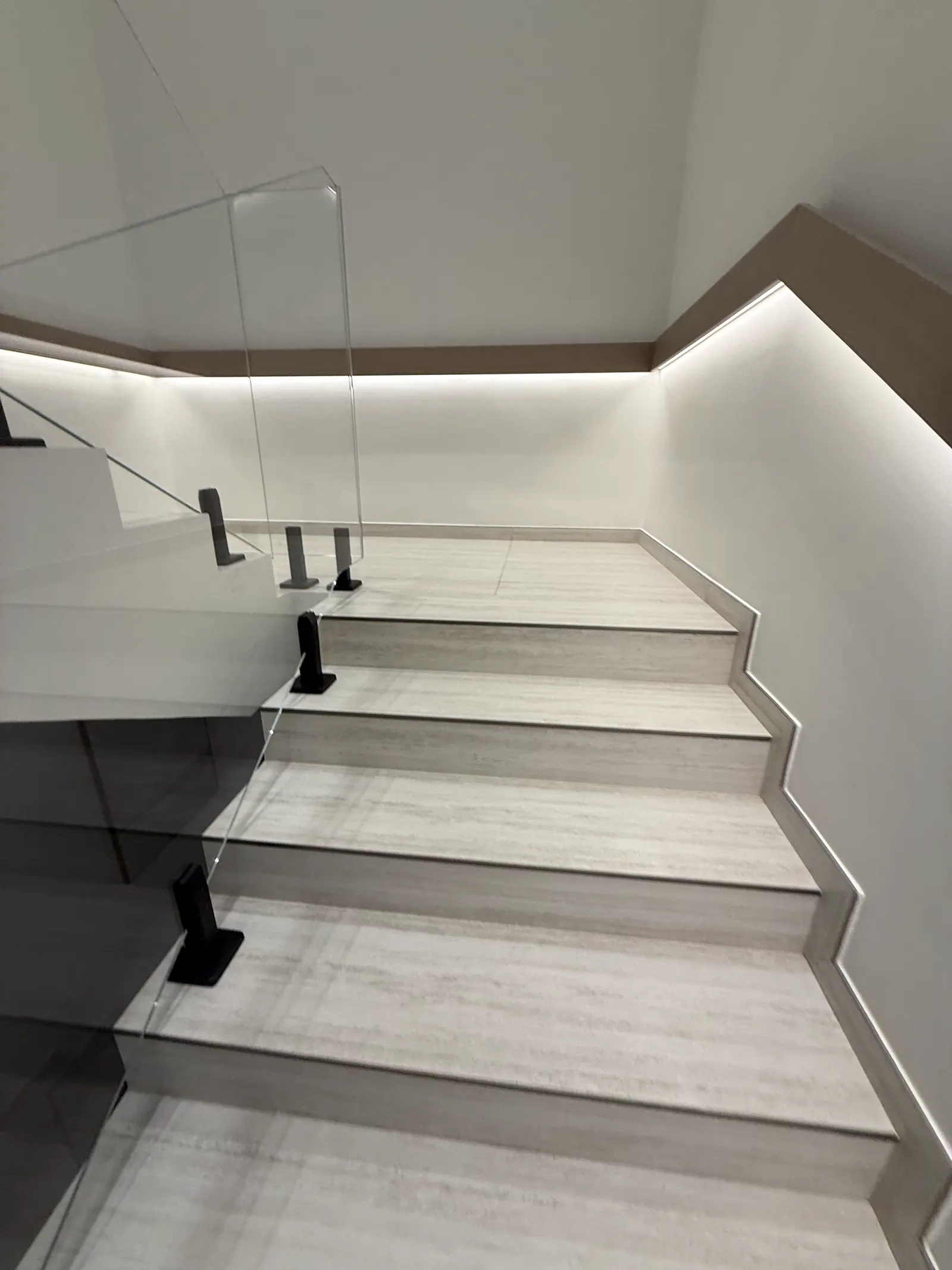 Stone staircase with a frameless glass balustrade and concealed cove lighting