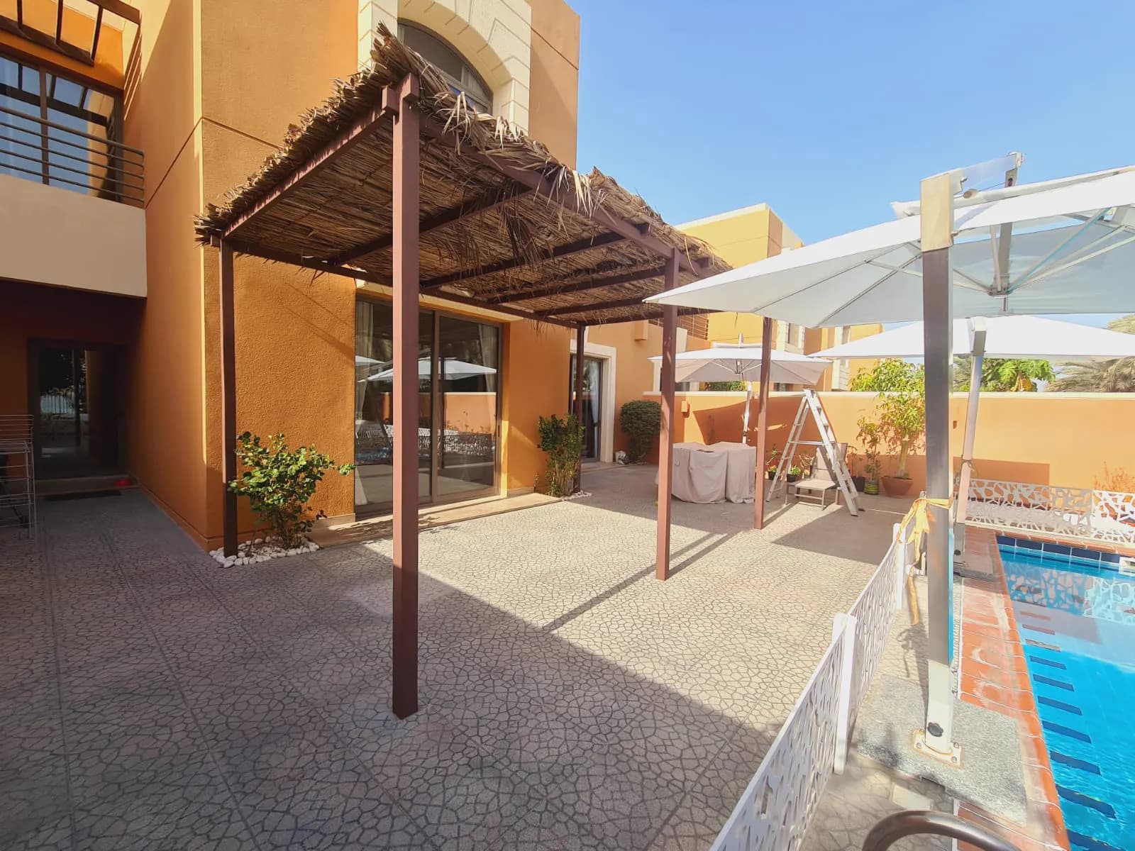 Palm-thatch pergola over a paved terrace with outdoor seating and parasols