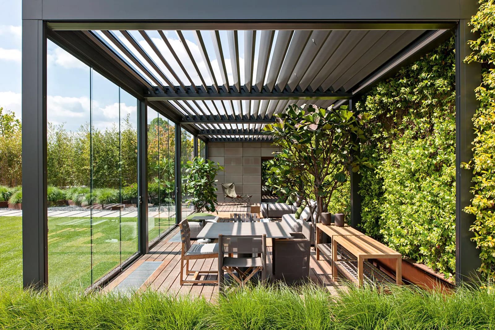 Aluminium louvred pergola over an outdoor dining terrace enclosed by planting