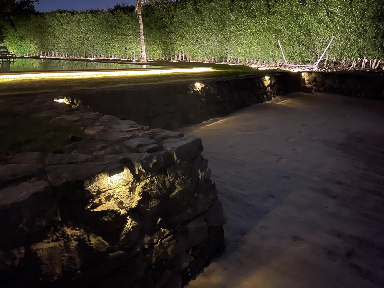 Stone retaining wall lit at night by recessed uplights along a garden path