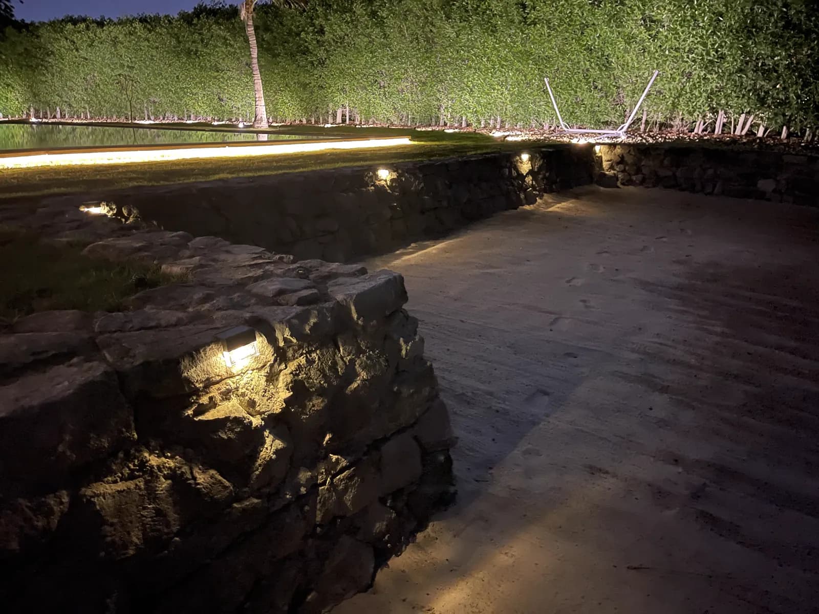 Night lighting washing a rough stone garden wall and the planting above it