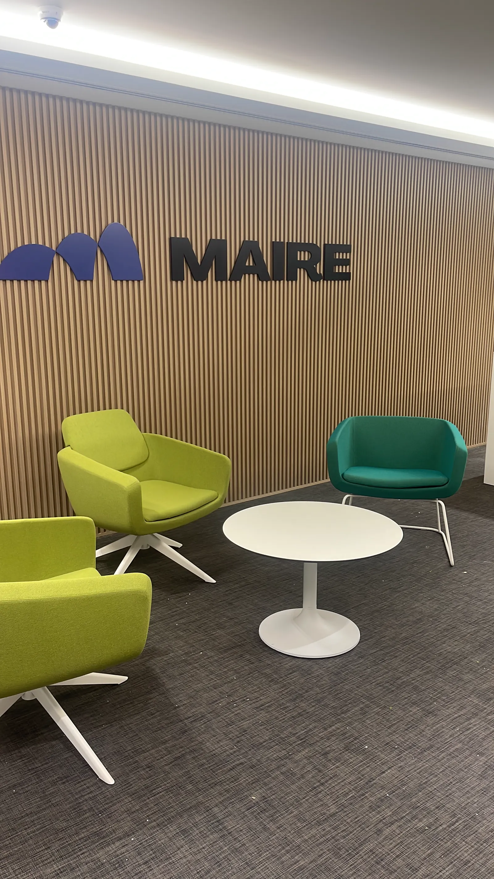 Maire Tecnimont waiting lounge with green and teal armchairs against a timber slat wall