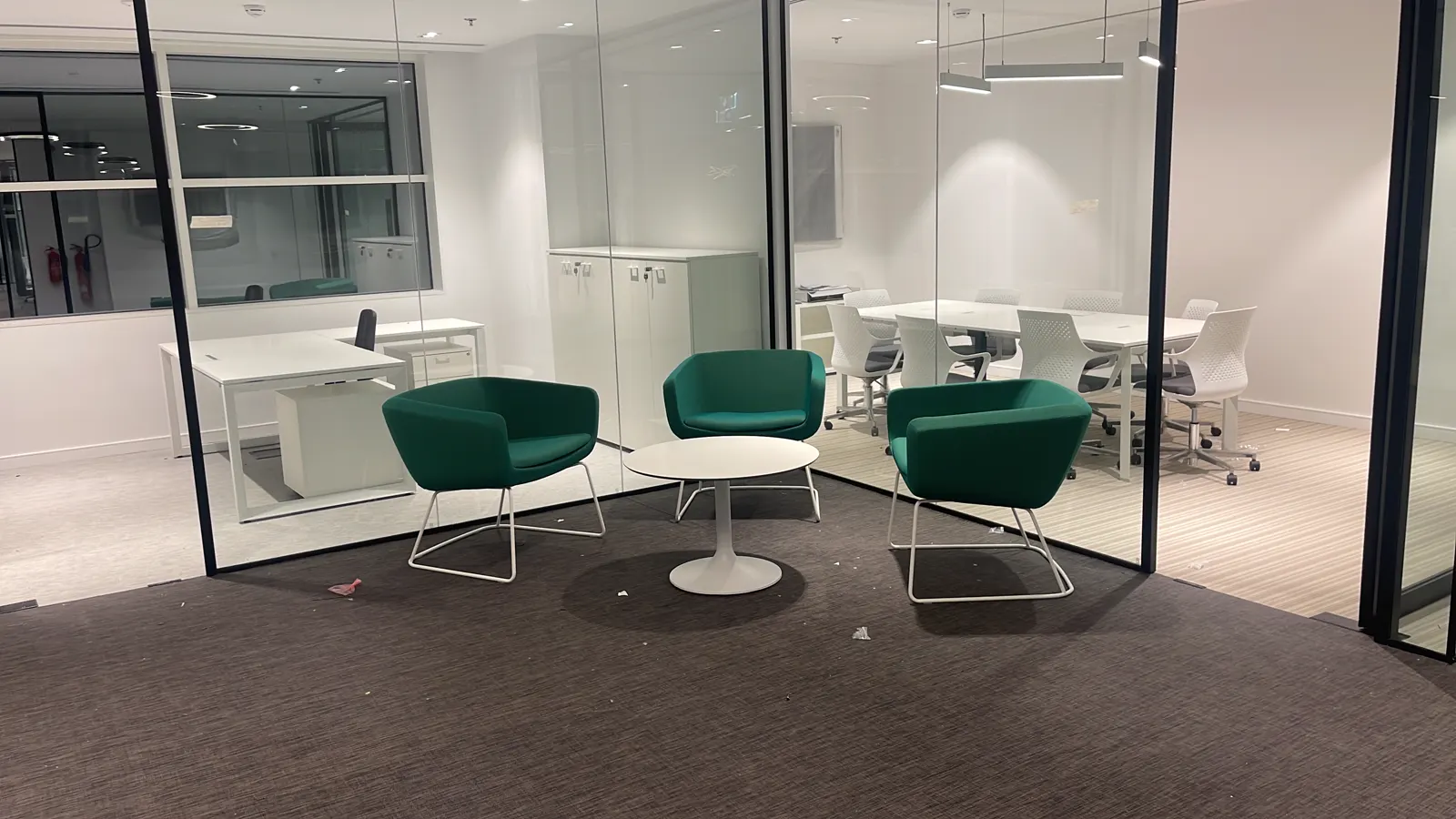 Meeting lounge with teal armchairs, glass partitions and acoustic ceiling