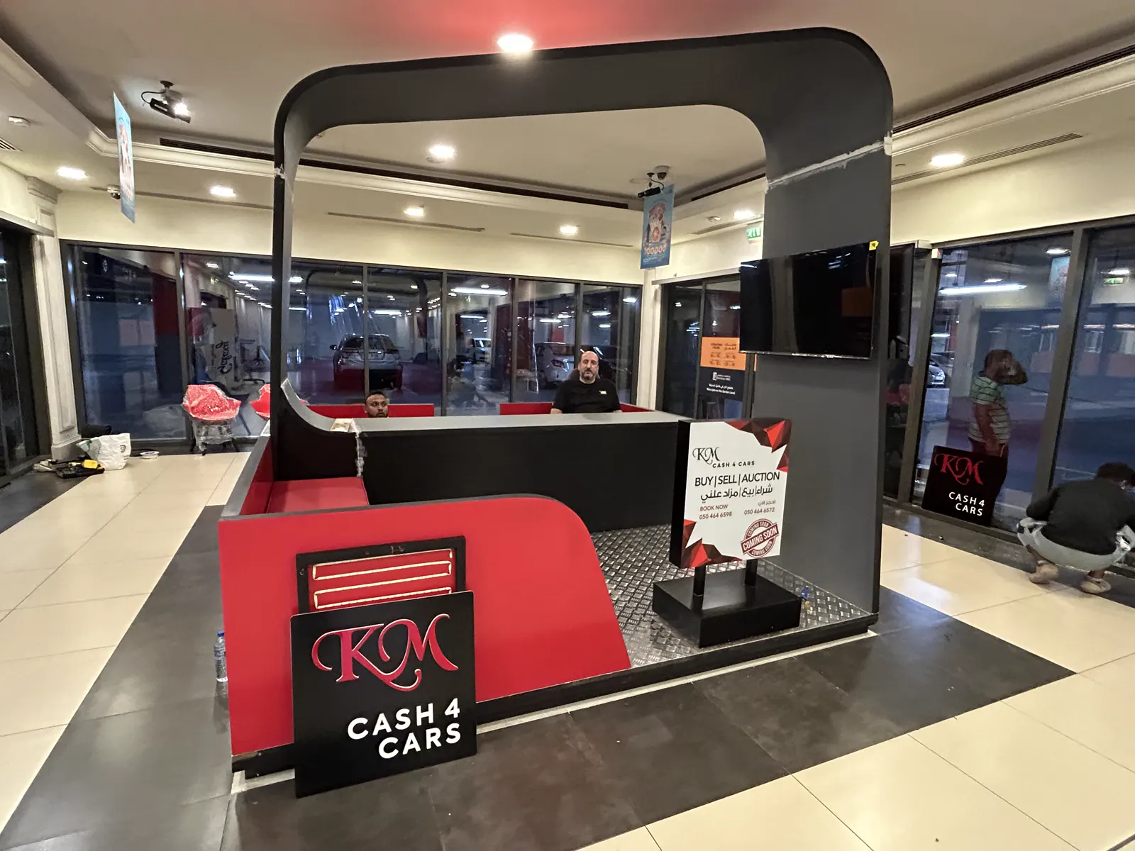 Freestanding retail kiosk in red and black with backlit brand signage in a mall concourse